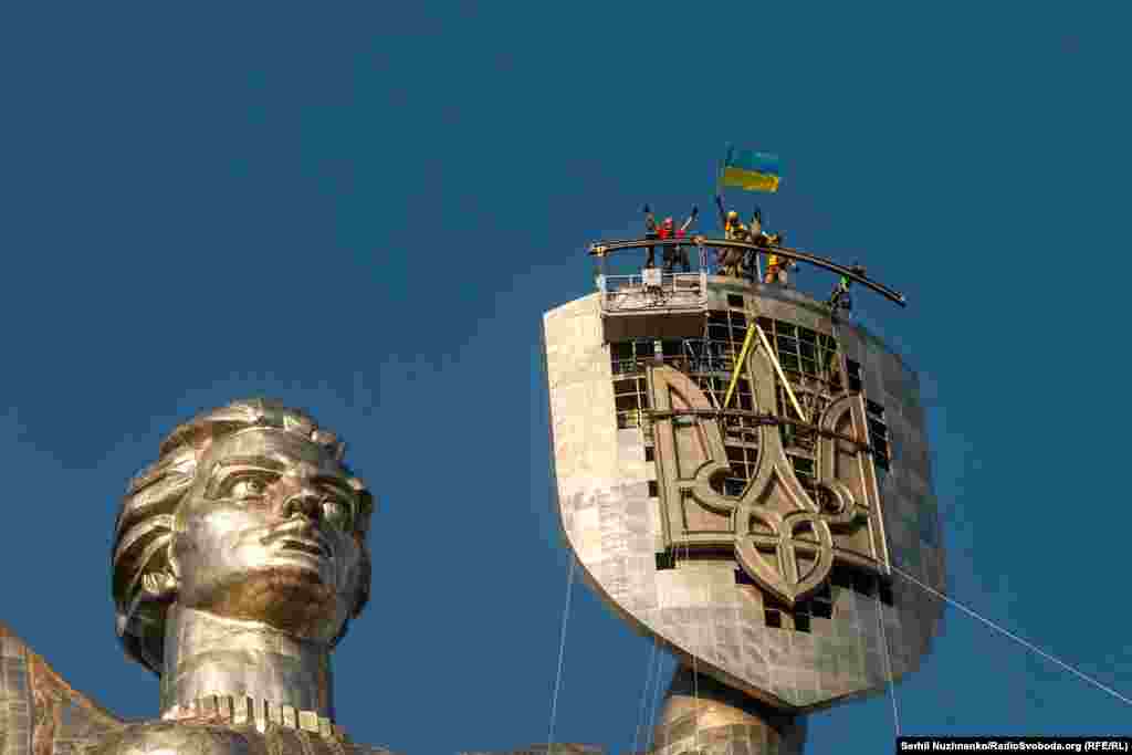 Рабочие отмечают установку украинского трезубца на щите монумента &laquo;Родина-мать&raquo; в Киеве, 6 августа 2023 года. Огромный трезубец заменил советский герб