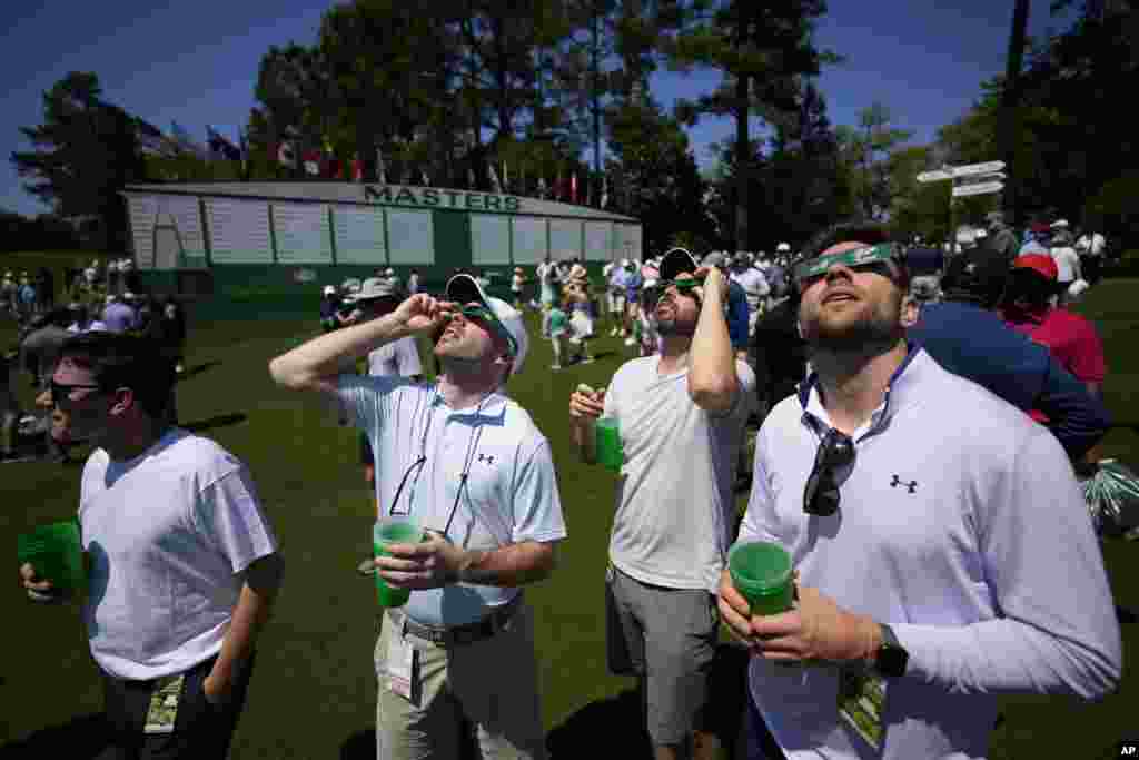 Augusta, Georgia, SUA - Jucătorii de golf se uită la eclipsa de soare în timpul unei runde de antrenament în pregătirea turneului de golf Masters de la Augusta National Golf Club 